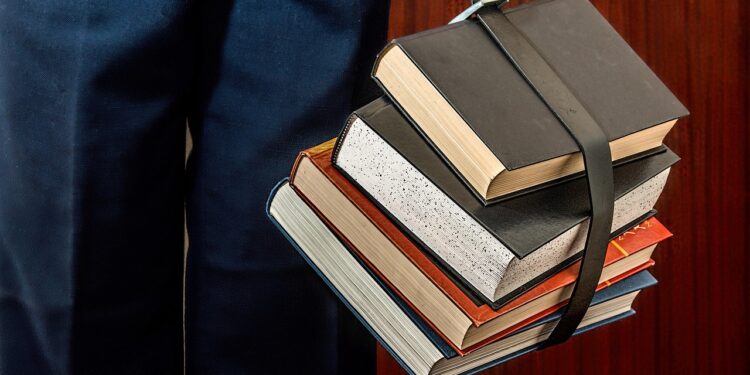A student studying beside a pile of books, illustrating the need for AI assessment before university AI curricula.