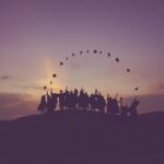 Graduates silhouetted against a sunrise throwing their caps in the air, illustrating the UK’s extended graduate visa policy.