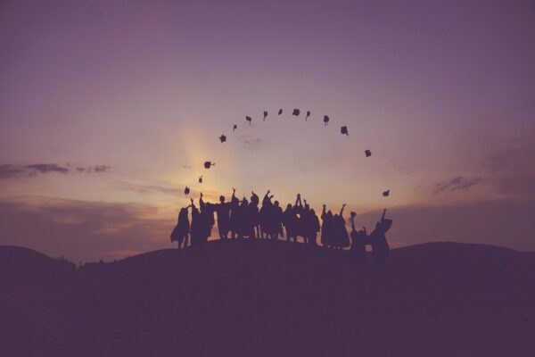 Graduates silhouetted against a sunrise throwing their caps in the air, illustrating the UK’s extended graduate visa policy.