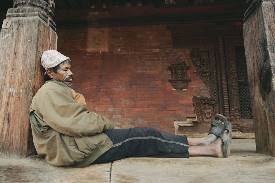 Elderly man resting with eyes closed beside an ancient temple, illustrating the article's winter relief theme.