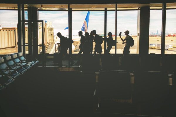 Travelers silhouetted at an airport gate with a skyline outside, illustrating rising airfare costs.