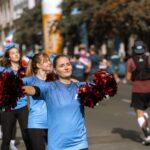 Cheerleaders in blue uniforms perform with red pom-poms at a street event, illustrating the Dallas Cowboys Cheerleaders' union representation.