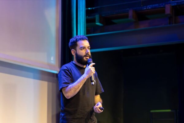Stock photo of A man presenting on stage with a microphone during a conference or event, used to illustrate this story on Cheyenne Jackson Launches Initiative to Help Actors Keep Insurance.