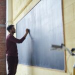 A man with dreadlocks writes on a blackboard in a classroom, illustrating Talarico's teaching background.