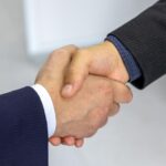 Two businessmen shaking hands in a close-up, illustrating the Salesforce-Rune Technologies acquisition agreement.