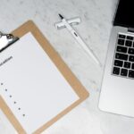 Stock photo of A clean and organized office desk setup featuring a laptop, clipboard with application form,, used to illustrate this story on UGC Window Closed; IITs Offer AI Degree Options.