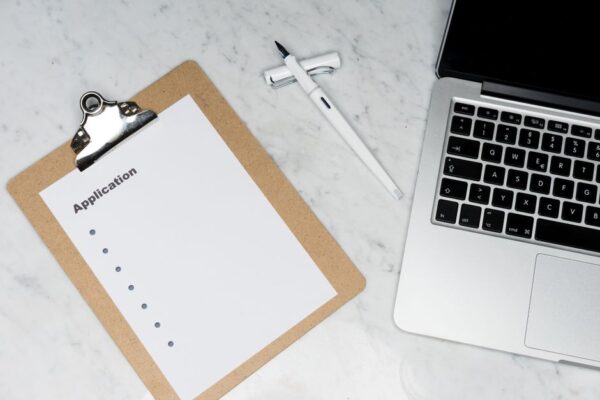 Stock photo of A clean and organized office desk setup featuring a laptop, clipboard with application form,, used to illustrate this story on UGC Window Closed; IITs Offer AI Degree Options.