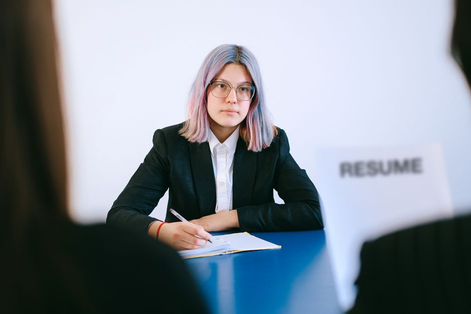 A suited woman writes notes during a job interview, illustrating discussion of vendor-driven enterprise software costs.