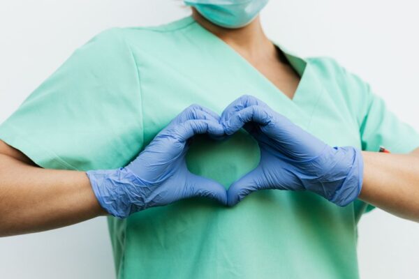 A nurse in blue gloves forms a heart shape with her hands, illustrating care in public sector jobs.