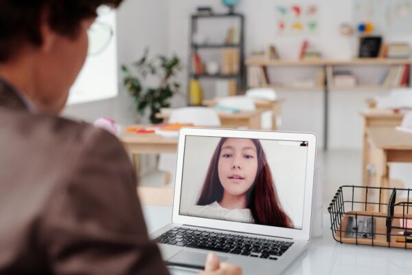 A teacher using a laptop for a virtual lesson with a female student on screen in a classroom, illustrating Jamia Millia Islamia's extended online classes.