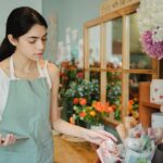 A florist checks an order on a tablet amid wrapped flowers, illustrating cash flow management in a small business.