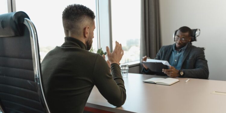 Two men speaking in a modern office interview setting, illustrating concerns about AI and junior technical hiring.