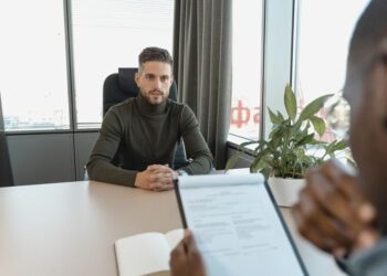 A professional man in a turtleneck sits at an office desk during an interview, illustrating enterprise software budget pressures.