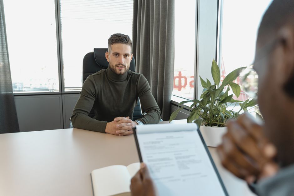 A professional man in a turtleneck sits at an office desk during an interview, illustrating enterprise software budget pressures.