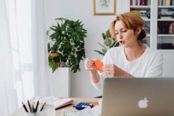 A woman reviews bills at a home desk with a laptop and plants, illustrating budget changes affecting energy bills and fuel costs.
