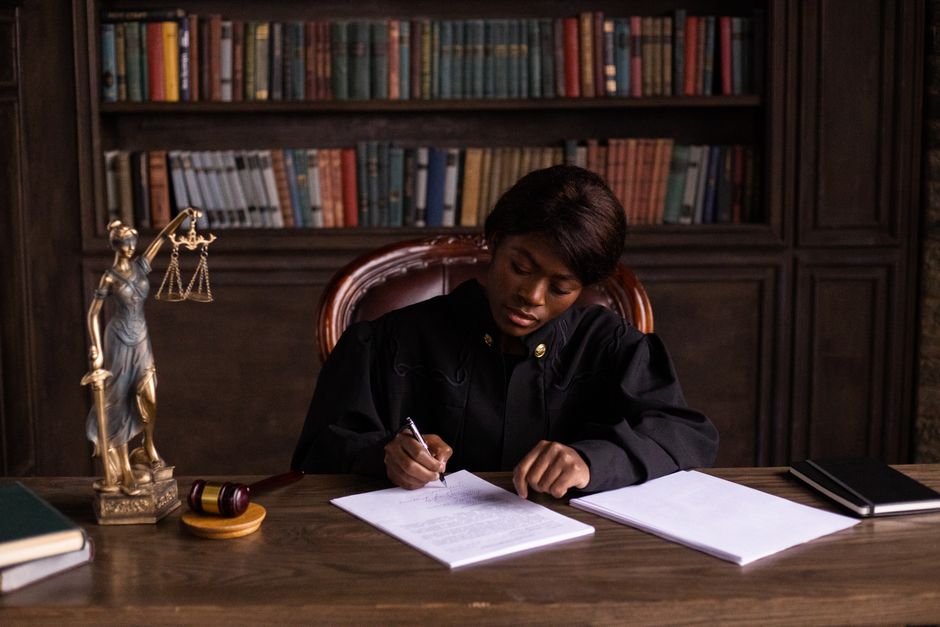 Stock photo of A judge in robes writing on a document at a desk in an office, used to illustrate this story on Cornell Prevails in DEI Hiring Lawsuit After Judge’s Finding.