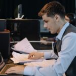 A young male professional working with a laptop and documents at an office desk, illustrating the Minnesota Daily's coverage of university cuts.