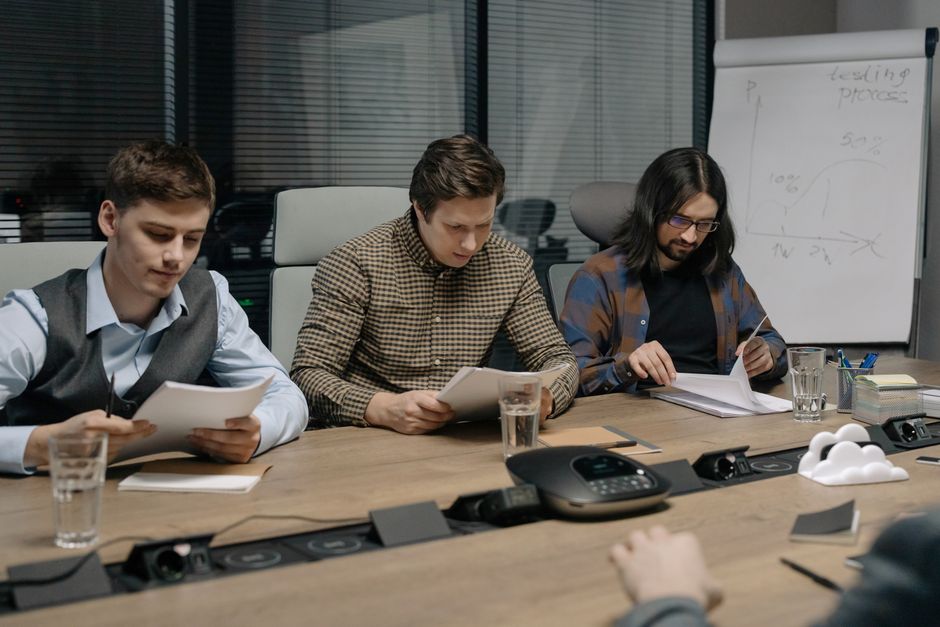 Stock photo of three business colleagues reviewing documents in a modern conference room during a daytime meeting, used to illustrate this story on TVS Motor Approves Consumer Finance Demerger.