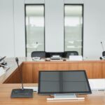 Stock photo of empty conference room setup with microphones, monitors, and sleek wooden tables ready for meetings, used to illustrate this story on Britain Sells Five-Year Debt at a 5.036% Yield.