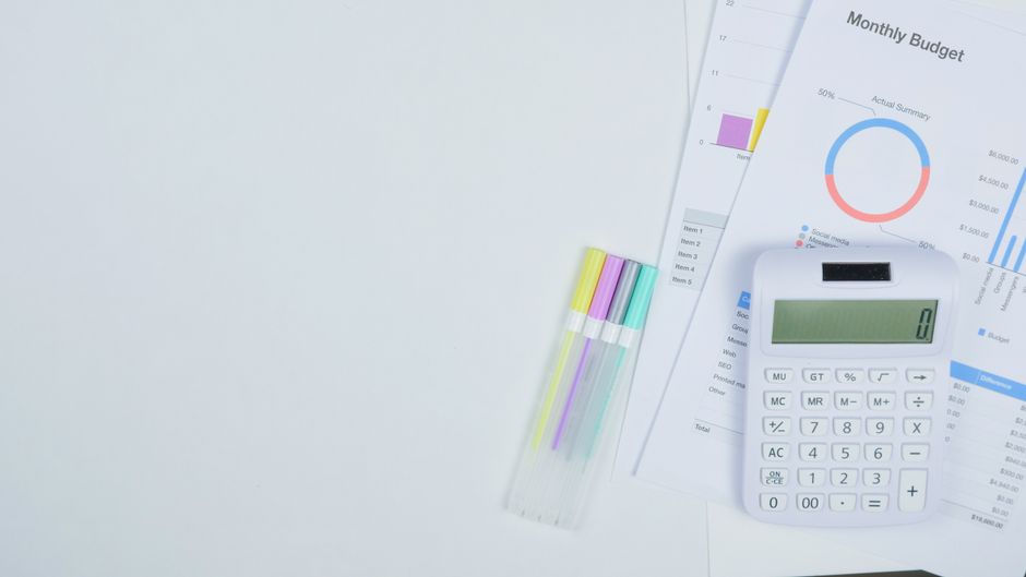 A minimalist office desk with a calculator and colorful pens, illustrating the budget planning behind Healey's funding announcement.