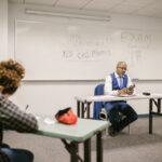 A proctor watches students taking tests in a classroom, illustrating the AP Sports Quota Teacher Recruitment exam.