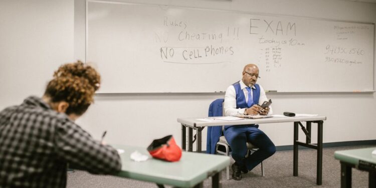 A proctor watches students taking tests in a classroom, illustrating the AP Sports Quota Teacher Recruitment exam.