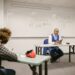 A proctor watches students taking tests in a classroom, illustrating the AP Sports Quota Teacher Recruitment exam.