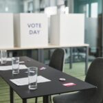 Stock photo of A prepared voting station with tables, chairs, and privacy booths in a conference room, used to illustrate this story on McMahon Plans $43,000 Education Office Furniture Purchase.