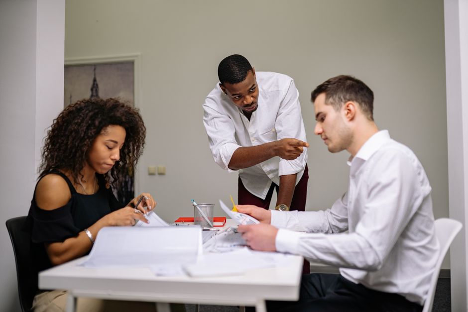 Stock photo of manager instructing employees during a focused team meeting in a modern office setting, used to illustrate this story on What to Do in Your First Ninety Days at a New Job.