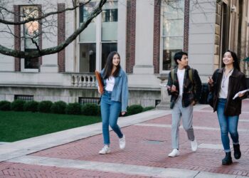 Young students walking along a campus sidewalk on a bright day, illustrating discussion of women’s exposure to AI.