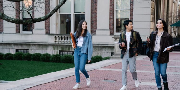 Young students walking along a campus sidewalk on a bright day, illustrating discussion of women’s exposure to AI.
