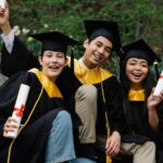 Three diverse graduates in caps and gowns holding diplomas outdoors, illustrating the student visa overhaul consultation.