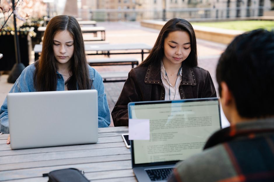 Stock photo of two students focus on studying with laptops at an outdoor university setting, promoting technology, used to illustrate this story on Students Face an AI Skills Gap as Employers Prize Collaboration.