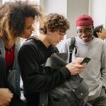 Stock photo of A group of diverse college students hanging out indoors and using a smartphone together, used to illustrate this story on How to Weigh Study Abroad’s Personal Value Against Its Cost.