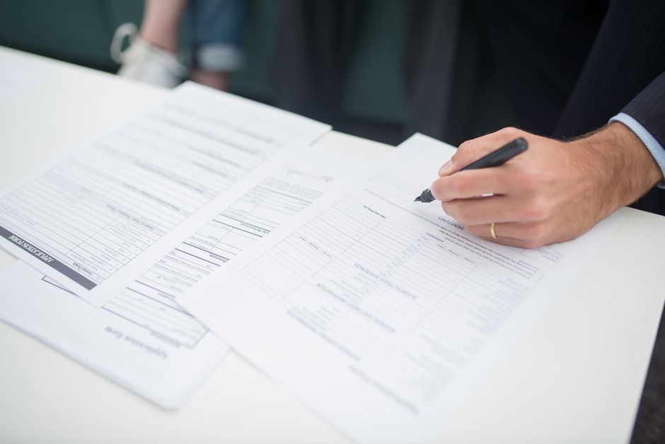 A hand signing insurance documents on a desk, illustrating the NPS Vatsalya rule updates.