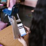 A student reads a book while using a smartphone in a classroom, illustrating modern educational challenges in campus placement preparation.
