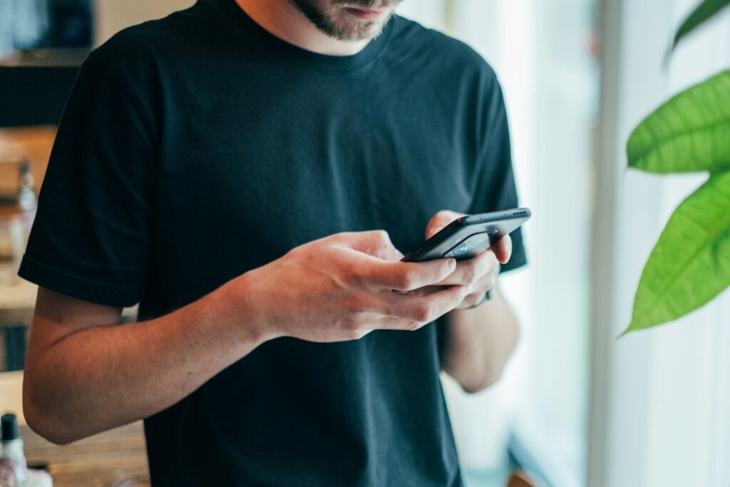 A man in a black crew-neck top using a smartphone, illustrating consumer-friendly AI agent tips.
