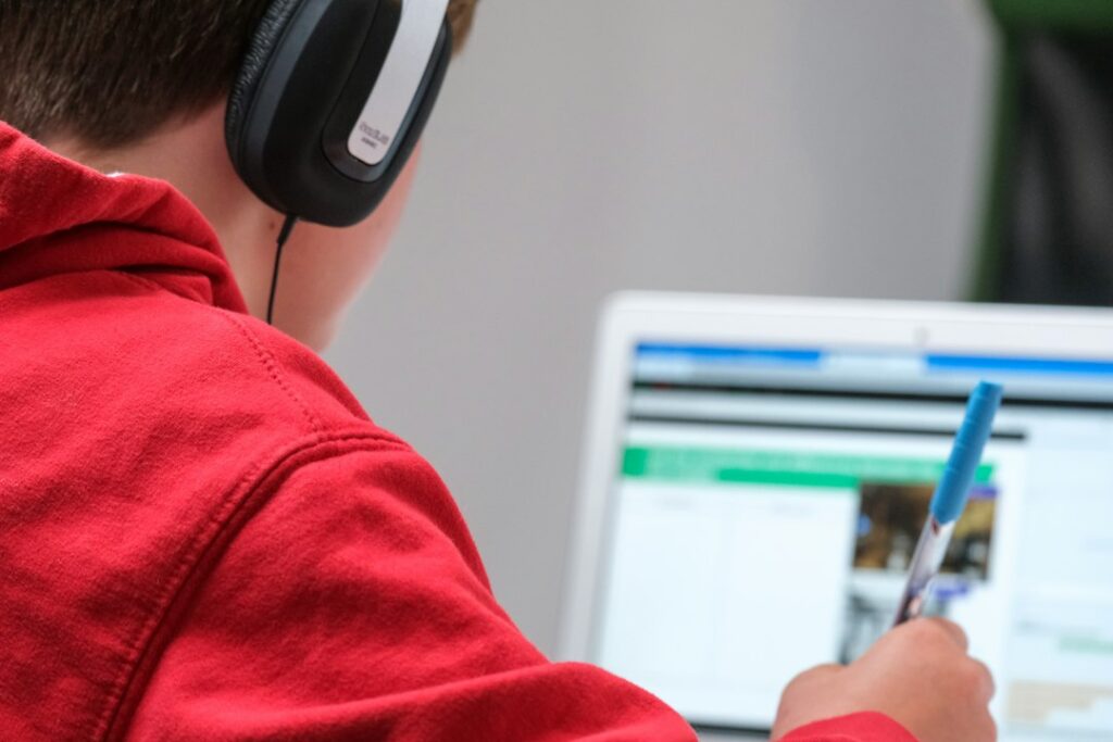 A person in a red shirt wearing black and gray headphones, illustrating the online classes at Jamia Millia Islamia.