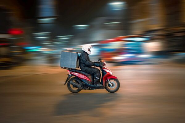 A delivery driver on a red scooter riding through a city at night, illustrating the DoorDash-Instacart deal.