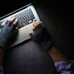A person wearing fingerless gloves typing on a laptop on a dark surface, illustrating the Binance crypto heist.