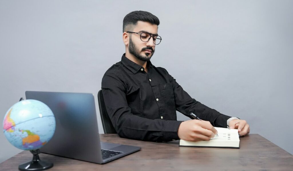 A man sits at a desk with a laptop and a globe, illustrating the setting for evaluating interview take-home tasks.