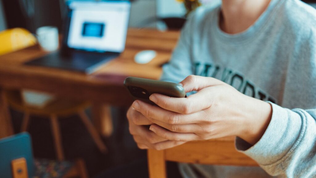 A person sitting at a table using a cell phone, illustrating social media use in the Meta settlement case.