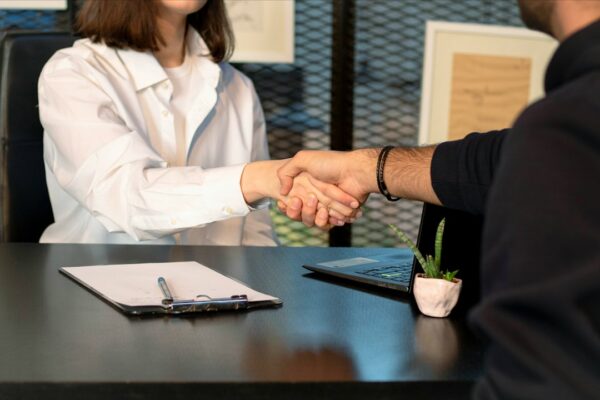 A man and a woman shaking hands in front of a laptop, illustrating workplace collaboration valued by employers.