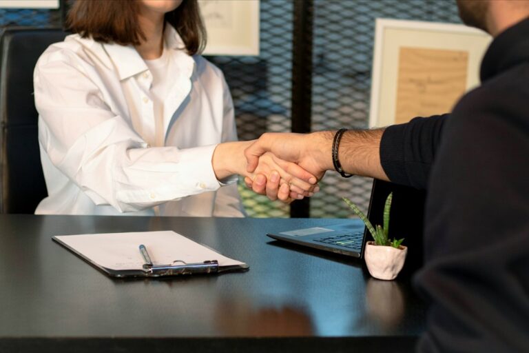 A man and a woman shaking hands in front of a laptop, illustrating workplace collaboration valued by employers.