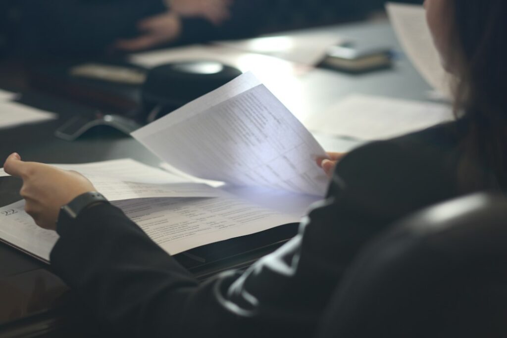A woman sitting at a table reading a paper, illustrating the process of evaluating interview take-home tasks.