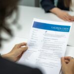 A woman reading a resume at a table, illustrating ethical preparation for a job interview.