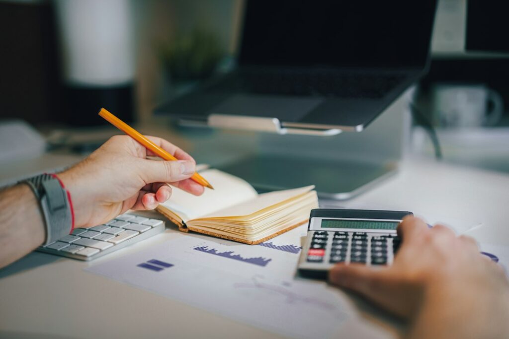 A person sitting at a desk with a calculator and a notebook, illustrating how to calculate your day rate before raising it.