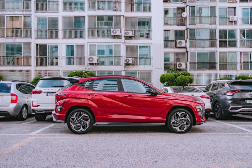 A red car parked in a lot with apartment buildings behind, illustrating the Hyundai Bayon launch article.