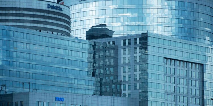 Glass skyscrapers reflecting the sky, showcasing brand logos under a calm sky.