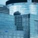 Glass skyscrapers reflecting the sky, showcasing brand logos under a calm sky.